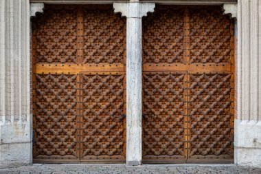 Entrika ile tasarlanmış bir çift ahşap kapı görkemli bir giriş sunuyor. Her panelde ayrıntılı geometrik desen var.