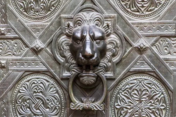 Tanınmış bir aslan başlı tokmağı olan süslü, metal bir kapı. Kapı karmaşık desenler ve ayrıntılı işçilik sergiliyor, görkemli bir görünüm veriyor..