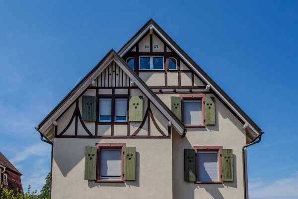 A charming, multi-story home displays architectural features. The pale fa?ade is adorned with decorative timber framing, complemented by green shutters.