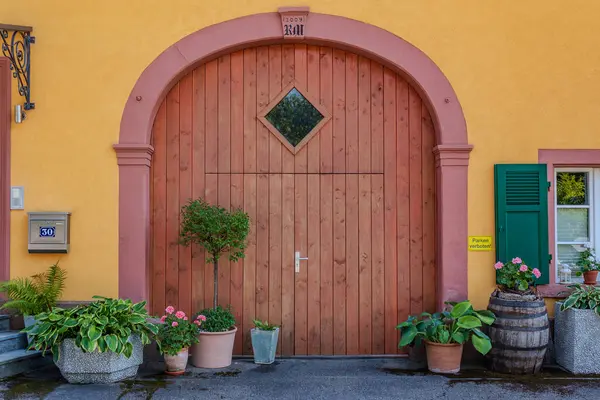 Yeşillik ve saksı bitkileriyle çevrili büyük ahşap kapılı büyüleyici bir bina, davetkar ve resimli bir giriş yaratıyor..