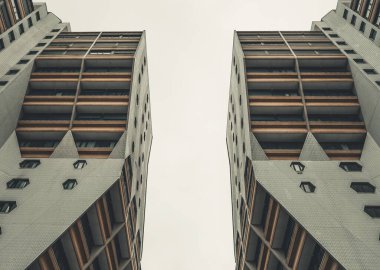 Eşsiz geometrik pencere şekilleri ve fayanslı cephesi olan iki modern kulenin yukarı perspektifi.