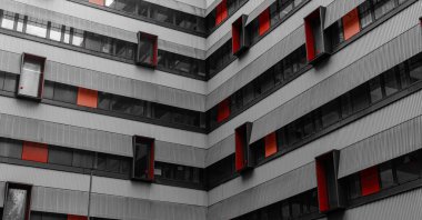 Kırmızı pencere aksanları ve çizgili dokuları olan modern bir binanın soyut cephesi, geometri ve tekrarları vurguluyor.