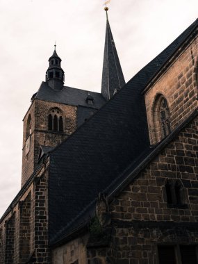 Karanlık tonlu gotik kilise mimarisi sarp kayrak çatıları ve belirgin bir kulesi var, bulutlu bir gökyüzünün altında fotoğraflanmış..