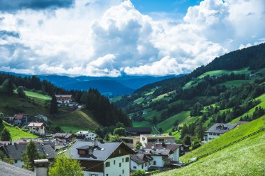 Yeşil tepelerde evleri olan Güney Tyrol 'da büyüleyici bir dağ köyü. Bulut oluşumları dağların üzerinde yükselir ve güzel bir vadi manzarası yaratır..