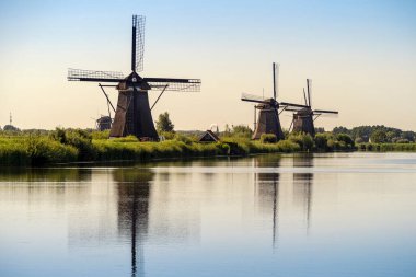 KINDERDIJK, NETHERLANDS - Temmuz 04, 2019 Sabahın erken saatlerinde kanala yansıyan tarihi yel değirmenleri