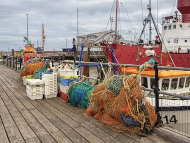 HARWICH, ESSEX, UK - AUGUST 12, 2018:  View of the harbour with nets and crates on the quay with fishing trawlers in the background