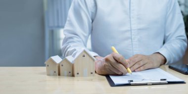 Ev modeli ve iş adamı satın alma ya da ipotek sözleşmesi imzalıyor. Gayrimenkul işlemleri, ev sigortası, ipotek kredisi anlaşması ve emlak yatırımı kavramı. Kopyalama alanı dahil.