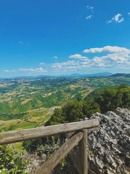 Büyüleyici yaz manzarası, panoramik tepeler, yeşil vadiler ve mavi gökyüzü, bir dağ tarafından ahşap çitle çekilmiş. Seyahat, turizm, özgürlük ve doğa temaları için ideal.