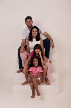 Tarafsız bir geçmişi olan mutlu ve sevgi dolu bir aile fotoğraf stüdyosunda poz veriyor. Gülümseyen anne onun yanındayken baba merdivenlerde oturur. Renkli kıyafetler içindeki iki kız önde, aileyi taşıyan neşeli bir ortam yaratıyorlar.