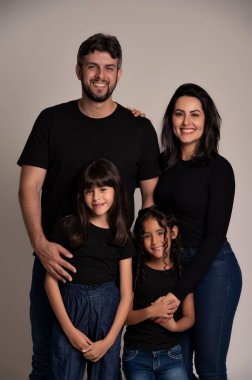 Bir ailenin duygusal portresi, gülümseyen ve kucaklayan, siyah tişörtler ve kotlar giyen, bir stüdyo ortamında onların mutlu yüzlerini vurgulayan sevgi ve birlik gösteren.