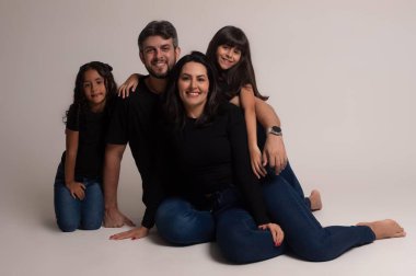 Güzel bir aile stüdyoda birlikte poz veriyor. Gülümseyen anne babaları ve iki neşeli kızı var. Tarafsız ortam onların duygusal bağlantılarını ve mutluluklarını vurguluyor, sevgi ve birliğin bir sahnesini yakalıyorlar..