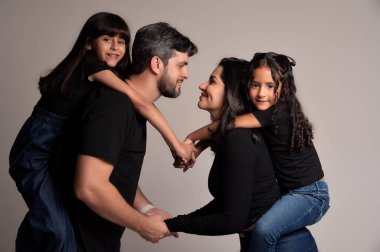 Birleşmiş bir ailenin sıcak ve sevgi dolu bir sahnesinde, bir anne ve baba sırtüstü oynaşırken birbirlerine sevgiyle bakarlar. Herkes günlük siyah ve mavi kıyafetler giyer, neşe ve beraberliği yansıtır..