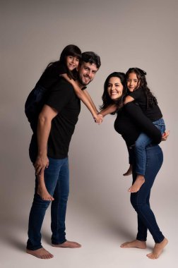 Çekici bir aile fotoğraf stüdyosunda poz veriyor, anne ve baba iki kızını omuzlarında taşıyor. Herkes gülümsüyor, sevgi ve neşe saçıyor. Çocuklar kot pantolon ve siyah tişört giyer, ebeveynler rahat, rahat kıyafetler giyer, kreatin