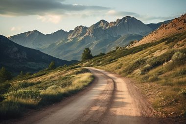 Döner toprak bir yol görkemli bir dağ sırasının içinden geçer, güneş ışığıyla yıkanır. Sakin manzara nefes kesici manzara, seyahat, macera ve doğa temaları için ideal..