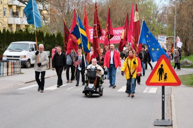 Nynashamn, İsveç - 1 Mayıs 12025: 1 Mayıs göstericileri İsveç, AB, BM ve kırmızı bayraklarla sınır kapısının önünden geçen çocukların yanından geçtiler. Protestocular sosyal reform ve işçi hakları talep ediyorlar.