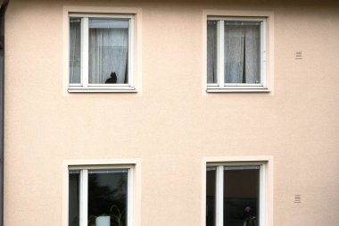 Stockholm, İsveç - 8 Mayıs 2025: Bej bir apartmanın pencere perdesinin arkasında oturan siyah bir kedi, şehir yaşamında her gün sakin bir an yaratıyor..