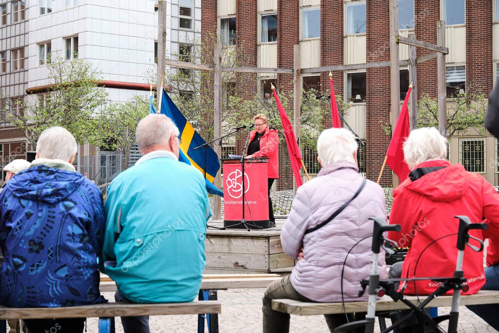 Nynashamn, Sweden - May 1 2025: Social Democratic speaker addresses seated audience during May Day event. Swedish and red flags visible, with senior attendees in foreground.