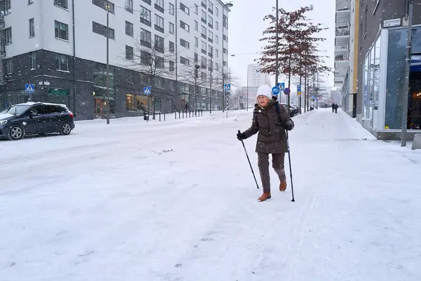Liljeholmen, Stockholm İlçesi, İsveç - 2 Ocak 2024: Karlı bir yaya yolunda çubuklarla yürüyen yaşlı kadın.