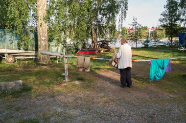 Nynashamn, Stockholm İlçesi, İsveç - 24 Mayıs 2024: Yaşlı bir kadın, deniz kenarındaki bir yol kapısından çamaşırları kuru ellerle yıkıyor. Minimalist ve basit bir hayatı sembolize etmek.