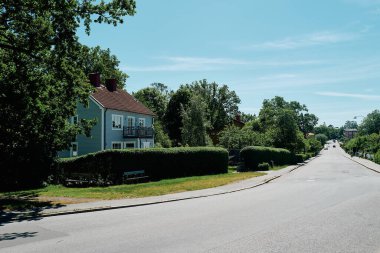Nynashamn, Stockholm County, İsveç - 14 Haziran 2024: Solunda bir ev ve sağında bir sıra ağaç olan sakin bir yerleşim yeri. Sokaklar boş ve gökyüzü temiz.