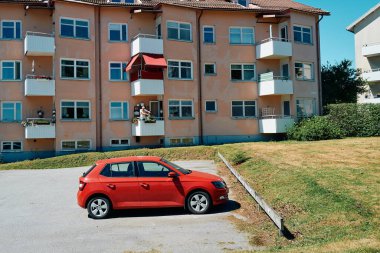 Nynashamn, Stockholm County, İsveç - 14 Haziran 2024: Bir binanın önüne park edilmiş kırmızı bir araba. Araba küçük bir hatchback ve kaldırıma yakın bir yere park edilmiş.