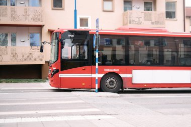 Nynashamn, Stockholm County, İsveç - 17 Nisan 2025: kırmızı bir otobüs caddeden geçiyor. Otobüs yaya geçidinden geçiyor.