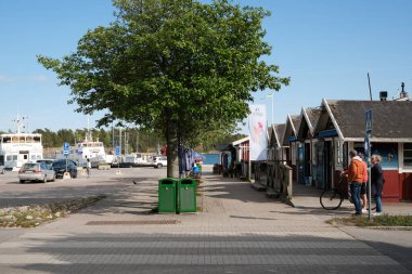 Nynashamn, Stockholm İlçesi, İsveç - 26 Mayıs 2025: Yanında yeşil bir çöp tenekesi olan bir ağaç kaldırımın ortasındadır. Bir adam kaldırımda bisikletle yürüyor.