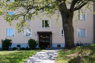 Nynashamn, Stockholm County, İsveç - 19 Mayıs 2025: önünde ağaç olan bir bina. Ağaç çıplak ve bina bej..