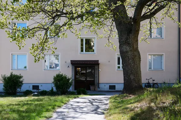 Nynashamn, Stockholm County, İsveç - 19 Mayıs 2025: önünde ağaç olan bir bina. Ağaç çıplak ve bina bej..