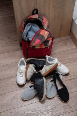 Renkli kırmızı kontrol edilmiş sırt çantası ve dağınık ayakkabılar bir çocuk odasında yerde yatıyor.