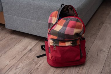 Odadaki yatağın yanında yerde duran kırmızı renkli kareli sırt çantası. Temizlik ve disiplin.