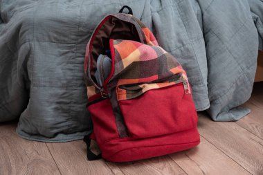 Odadaki yatağın yanında yerde duran kırmızı renkli kareli sırt çantası. Temizlik ve disiplin.