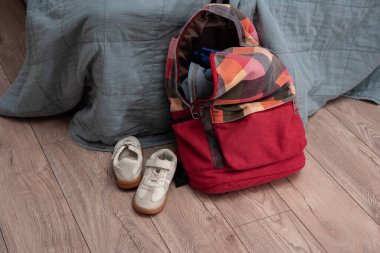 Beyaz bir çift çocuk ayakkabısı ve kırmızı renkli bir sırt çantası odanın zemininde yatıyor. Temizlik ve disiplin. Dökülüyor
