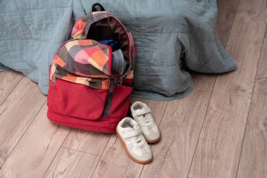 Beyaz bir çift çocuk ayakkabısı ve kırmızı renkli bir sırt çantası odanın zemininde yatıyor. Temizlik ve disiplin. Dökülüyor