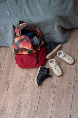 iki çift çocuk ayakkabısı ve kırmızı renkli bir sırt çantası odanın zemininde yatıyor. Temizlik ve disiplin. Dökülüyor