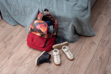 iki çift çocuk ayakkabısı ve kırmızı renkli bir sırt çantası odanın zemininde yatıyor. Temizlik ve disiplin. Dökülüyor