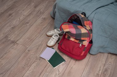 Bir çift çocuk ayakkabısı, dağınık kitaplar ve odanın zemininde kırmızı renkli bir sırt çantası var. Temizlik ve disiplin. Dökülüyor