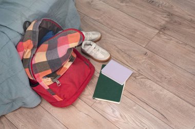 Bir çift çocuk ayakkabısı, dağınık kitaplar ve odanın zemininde kırmızı renkli bir sırt çantası var. Temizlik ve disiplin. Dökülüyor