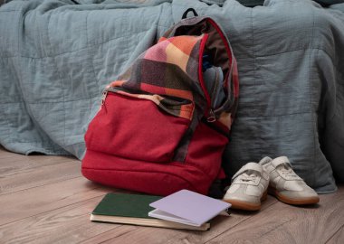 Bir çift çocuk ayakkabısı, dağınık kitaplar ve odanın zemininde kırmızı renkli bir sırt çantası var. Temizlik ve disiplin. Dökülüyor