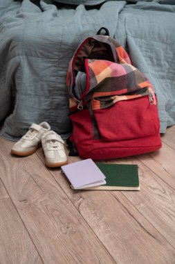 Bir çift çocuk ayakkabısı, dağınık kitaplar ve odanın zemininde kırmızı renkli bir sırt çantası var. Temizlik ve disiplin. Dökülüyor