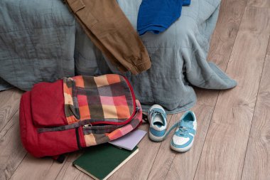 Giysiler yatağa saçılmış. Bir çift çocuk ayakkabısı, dağınık kitaplar ve odanın zemininde rengarenk bir sırt çantası. Temizlik ve disiplin. Dökülüyor.