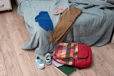 Giysiler yatağa saçılmış. Bir çift çocuk ayakkabısı, dağınık kitaplar ve odanın zemininde rengarenk bir sırt çantası. Temizlik ve disiplin. Dökülüyor.