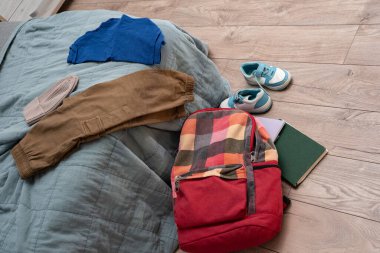 Giysiler yatağa saçılmış. Bir çift çocuk ayakkabısı, dağınık kitaplar ve odanın zemininde rengarenk bir sırt çantası. Temizlik ve disiplin. Dökülüyor.