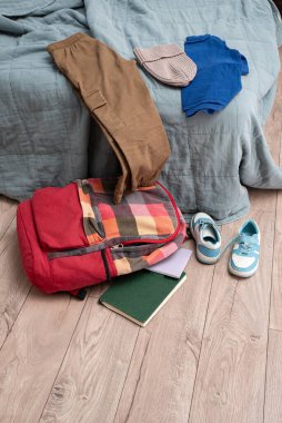 Giysiler yatağa saçılmış. Bir çift çocuk ayakkabısı, dağınık kitaplar ve odanın zemininde rengarenk bir sırt çantası. Temizlik ve disiplin. Dökülüyor.