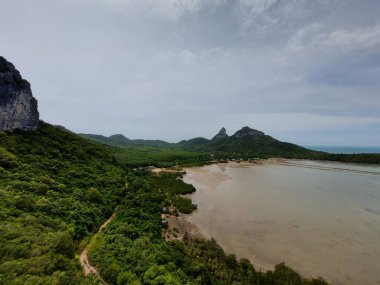 Yeşilliklerle çevrili güzel bir dağ manzarası ve arka planda bulutlu mavi bir gökyüzü.