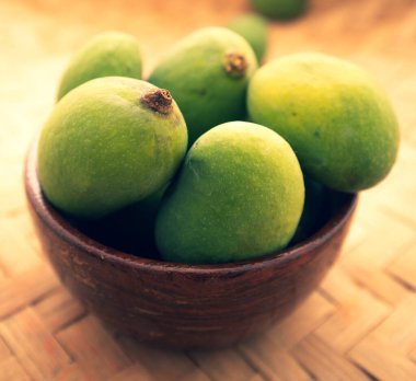 Taze yeşil mango kırsal kahverengi bir kasede dinleniyor, doğal durgun yaşam kompozisyonu..