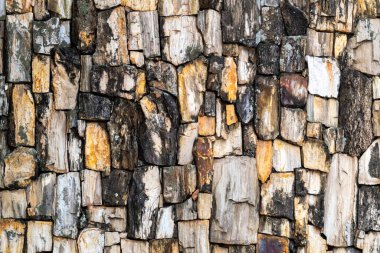 Düzensiz şekilli, toprak tonlu doğal taşlardan oluşan desenli duvar, kırsal ve organik bir görünüm yaratıyor..