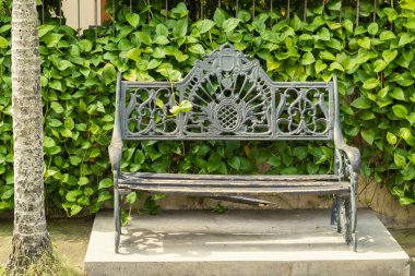 Süslü demir parkı bankı yemyeşil bir yeşillik zemininde duruyor..