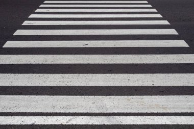 Zebra asfalt bir yolda geçiyor, beyaz boyalı şeritler ve koyu asfalt yüzeyi arasındaki kontrastı gösteriyor..