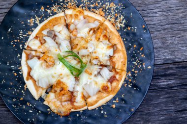 Karides ve mantarlı küçük bir pizzanın yukarıdan görünüşü, dilimlere ayrılmış, koyu bir tabakta, baharatlı..